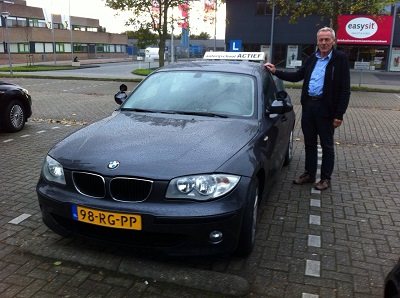 De rijinstructeur van Autorijschool Actief naast de BMW lesauto bij het examencentrum