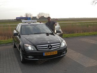 De rijinstructeur van Autorijschool Actief naast de zwarte Mercedes lesauto