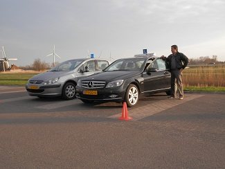De rijinstructeur van Autorijschool Actief bij de lesauto op een oefenterrein met pylonen