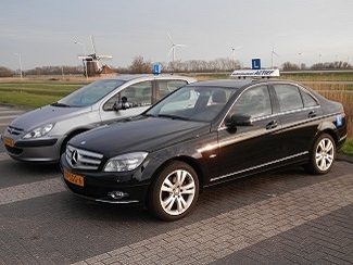 De zwarte Mercedes C220 CDI lesauto van Autorijschool Actief op een polderweg bij Bolsward, met een windmolen op de achtergrond