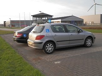 De zilvergrijze Peugeot 307 lesauto van Autorijschool Actief met een windmolen op de achtergrond